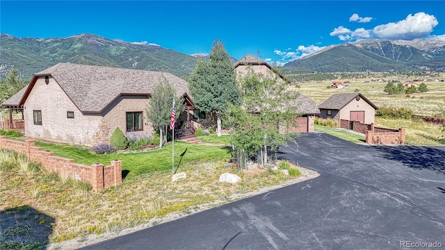 view of front of property with a mountain view, stone siding, a front yard, and driveway
