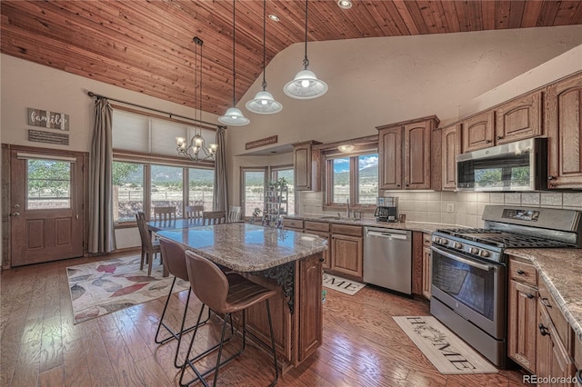 kitchen featuring light stone countertops, stainless steel appliances, wooden ceiling, decorative backsplash, and a kitchen island