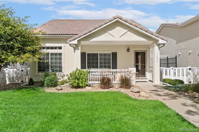 view of front facade with a front lawn, fence, a tile roof, and stucco siding