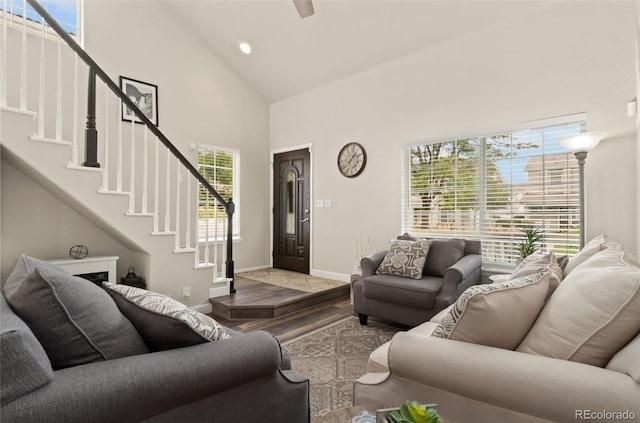 living room featuring high vaulted ceiling, light wood-style floors, baseboards, and stairs