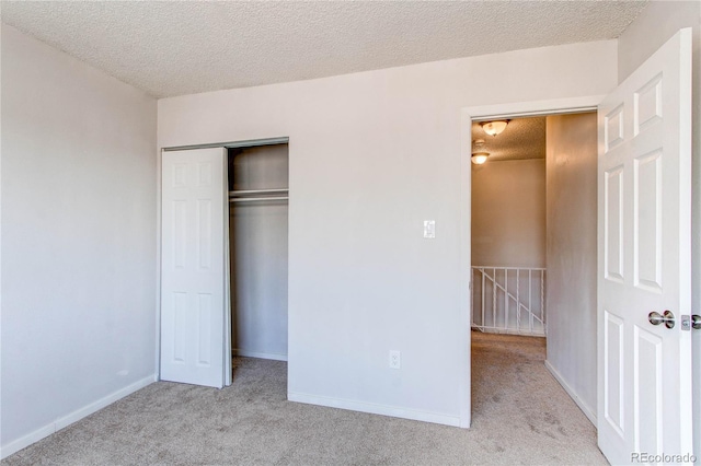 unfurnished bedroom featuring a textured ceiling, a closet, and light colored carpet