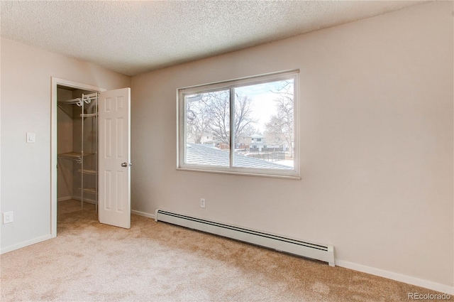 unfurnished bedroom featuring light carpet, a baseboard heating unit, a spacious closet, and a textured ceiling