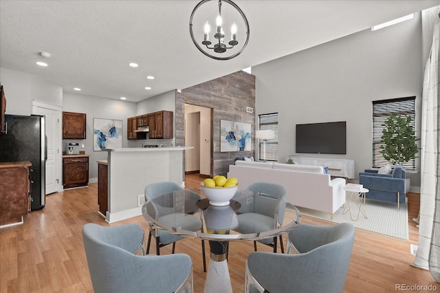 dining area with light wood finished floors, an accent wall, baseboards, recessed lighting, and a notable chandelier