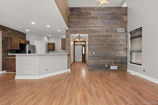 kitchen featuring light wood finished floors, stainless steel fridge with ice dispenser, visible vents, and wood walls