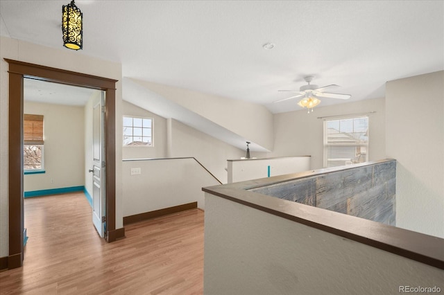 hallway with baseboards, an upstairs landing, and light wood-style floors