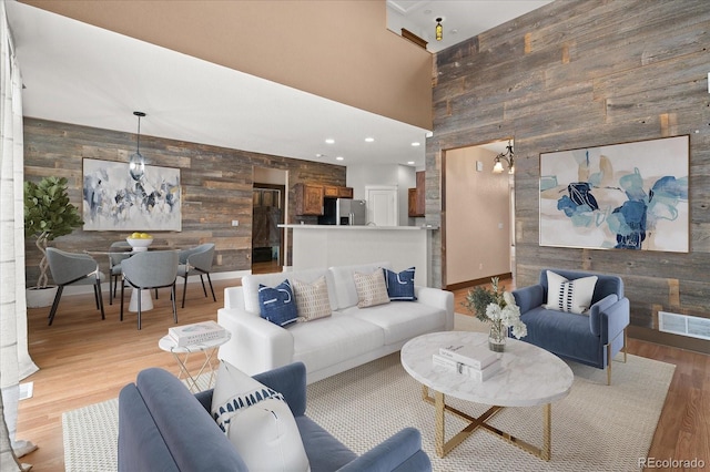 living room with light wood-type flooring, visible vents, wooden walls, a towering ceiling, and an accent wall