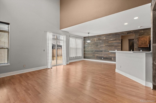 unfurnished living room with wooden walls, baseboards, a high ceiling, an accent wall, and light wood-type flooring