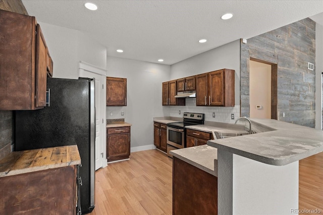 kitchen featuring a peninsula, a sink, light wood-style floors, under cabinet range hood, and appliances with stainless steel finishes