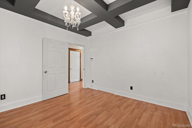 empty room featuring an inviting chandelier, light wood-style flooring, baseboards, and coffered ceiling