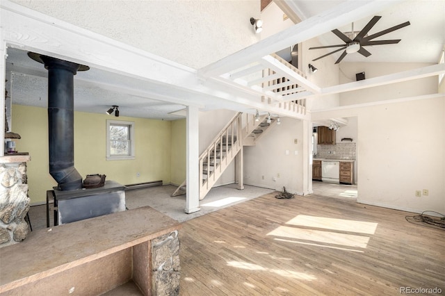 living room with a baseboard radiator, a ceiling fan, a wood stove, wood finished floors, and stairs