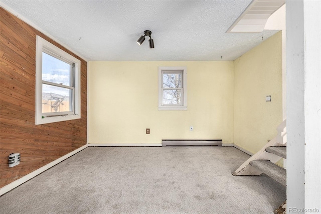 carpeted empty room with a baseboard heating unit, stairway, wood walls, and a textured ceiling