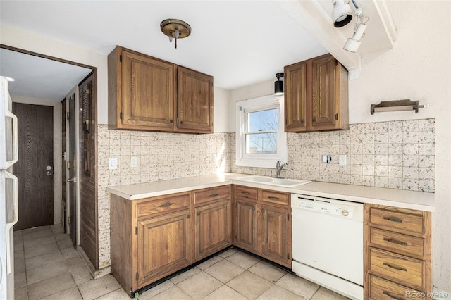 kitchen featuring brown cabinetry, decorative backsplash, white dishwasher, light countertops, and a sink