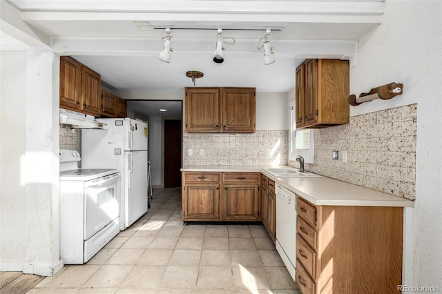 kitchen featuring white appliances, under cabinet range hood, brown cabinetry, and a sink