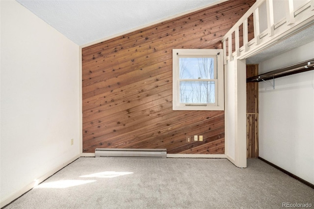 unfurnished bedroom featuring a closet, baseboard heating, carpet flooring, wooden walls, and baseboards