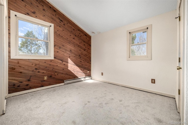 carpeted spare room featuring lofted ceiling, wood walls, and plenty of natural light