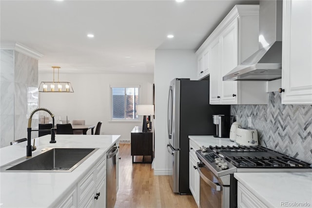 kitchen with pendant lighting, wall chimney range hood, sink, appliances with stainless steel finishes, and white cabinetry