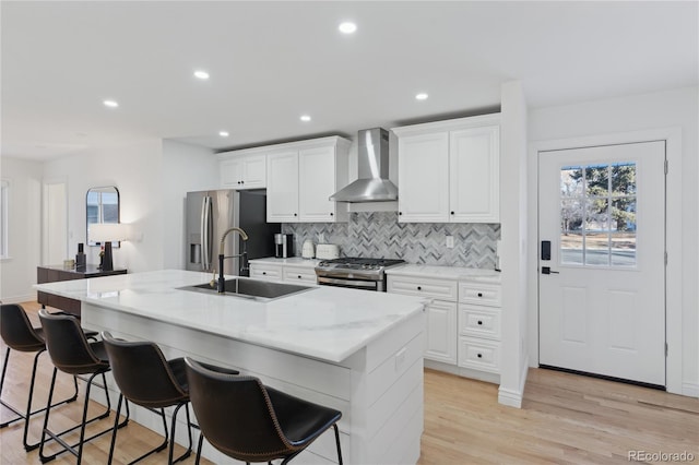 kitchen featuring appliances with stainless steel finishes, white cabinetry, sink, a center island with sink, and wall chimney exhaust hood