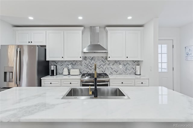 kitchen featuring wall chimney range hood, sink, appliances with stainless steel finishes, white cabinets, and decorative backsplash