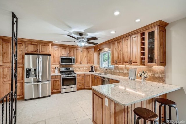 kitchen with sink, light stone counters, kitchen peninsula, a kitchen bar, and appliances with stainless steel finishes