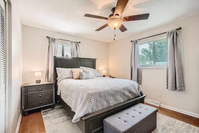 bedroom featuring multiple windows, ceiling fan, dark hardwood / wood-style flooring, and a textured ceiling