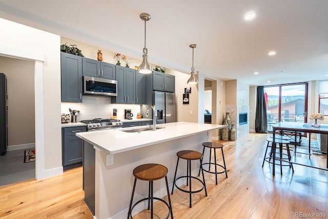 kitchen with an island with sink, sink, appliances with stainless steel finishes, a kitchen breakfast bar, and light wood-type flooring