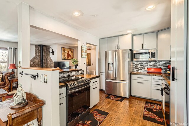 kitchen with dark countertops, hardwood / wood-style flooring, tasteful backsplash, and appliances with stainless steel finishes