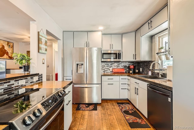 kitchen featuring stainless steel appliances, a sink, hardwood / wood-style floors, tasteful backsplash, and dark countertops