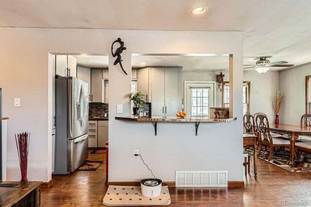 kitchen with stainless steel fridge, visible vents, decorative backsplash, dark wood finished floors, and a breakfast bar area