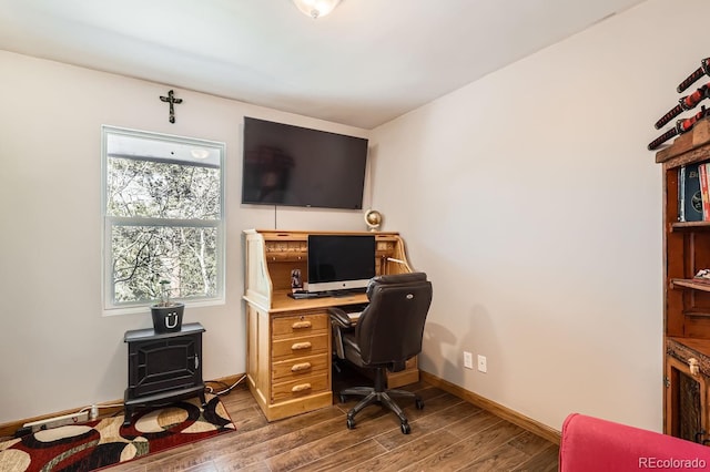 office area featuring a wood stove, baseboards, and wood finished floors