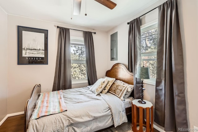 bedroom featuring multiple windows, wood finished floors, electric panel, and baseboards