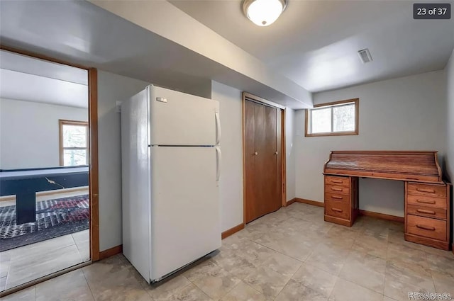 kitchen featuring baseboards, brown cabinets, and freestanding refrigerator