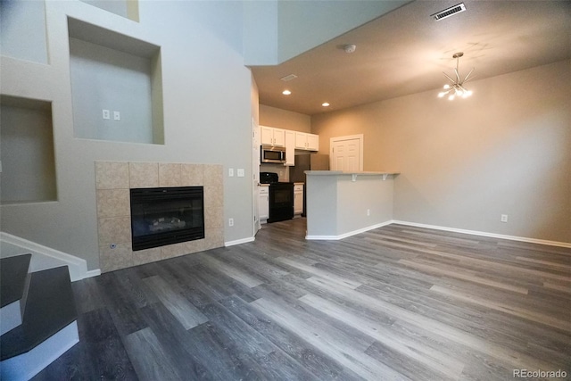 unfurnished living room with wood-type flooring, a tile fireplace, and a chandelier