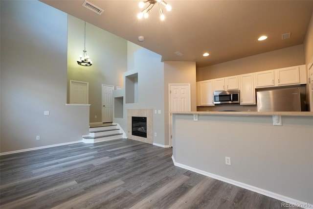 kitchen with fridge, a high ceiling, a tiled fireplace, dark hardwood / wood-style floors, and white cabinetry