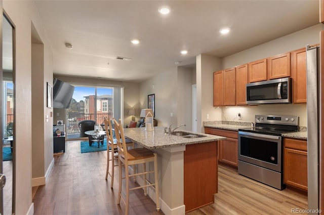 kitchen with open floor plan, appliances with stainless steel finishes, a sink, and light wood finished floors
