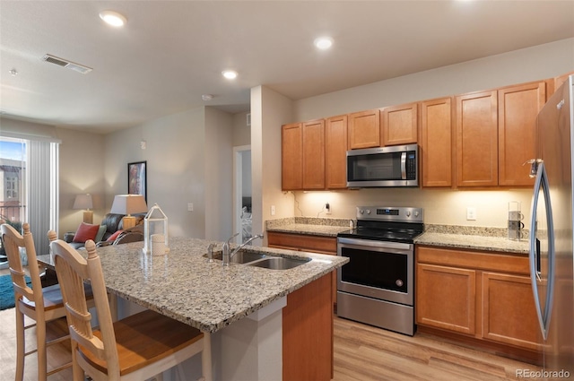 kitchen with a sink, a kitchen island with sink, light wood-type flooring, stainless steel appliances, and visible vents