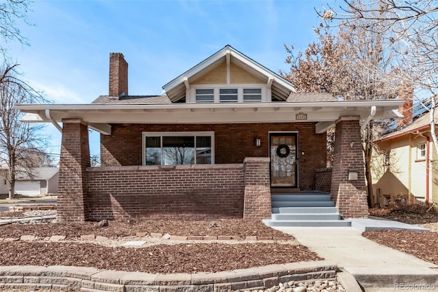 bungalow-style home with a porch, brick siding, and a chimney