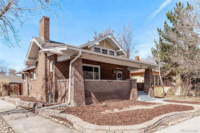 view of front of property with brick siding, a porch, and a chimney