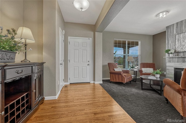 foyer with a tile fireplace, light wood-type flooring, baseboards, and a textured wall