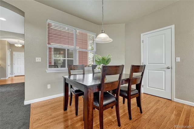 dining room featuring arched walkways, baseboards, light wood-type flooring, and a textured wall