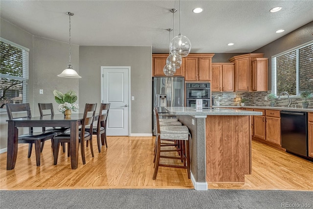 kitchen with light wood-type flooring, a kitchen island, brown cabinetry, and black appliances