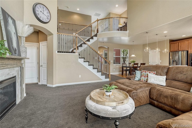 living area featuring visible vents, baseboards, stairway, arched walkways, and dark colored carpet