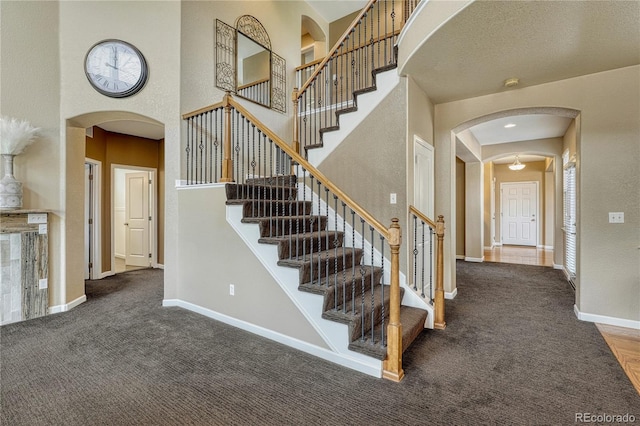 stairs featuring carpet, a towering ceiling, and arched walkways