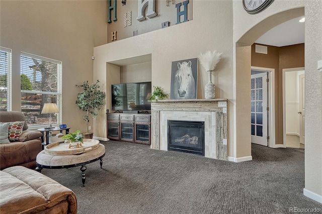 living area featuring baseboards, carpet flooring, a glass covered fireplace, visible vents, and arched walkways
