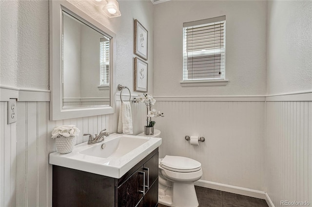 half bathroom featuring toilet, wainscoting, and vanity