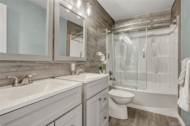 full bath with enclosed tub / shower combo, wood finished floors, two vanities, and a sink