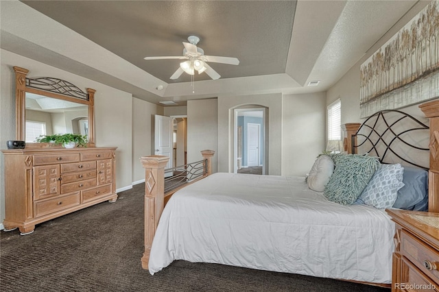 bedroom with a tray ceiling, dark carpet, visible vents, baseboards, and arched walkways