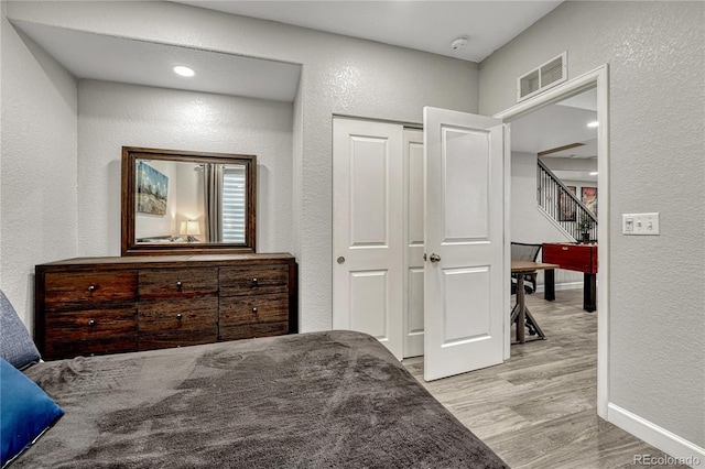 bedroom with visible vents, light wood-style flooring, and a textured wall