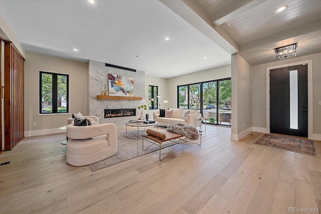 living room with light wood-type flooring, a stone fireplace, and a healthy amount of sunlight