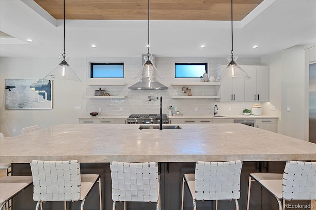 kitchen featuring wall chimney exhaust hood, white cabinetry, hanging light fixtures, a large island, and a breakfast bar