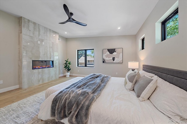 bedroom with ceiling fan, light hardwood / wood-style floors, and a fireplace